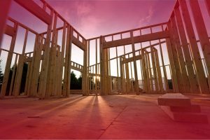 Low-angle view of a new home's wooden skeletal framing against a vibrant pink and orange sunset sky.