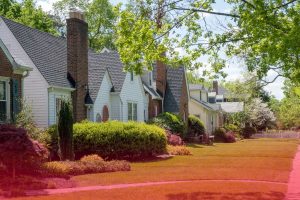 A quiet suburban street lined with a variety of single-family home property types, green lawns, and mature trees.